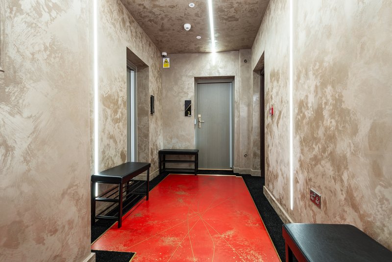 Industrial corridor with red floor, metal benches, grey doors and fluorescent lighting