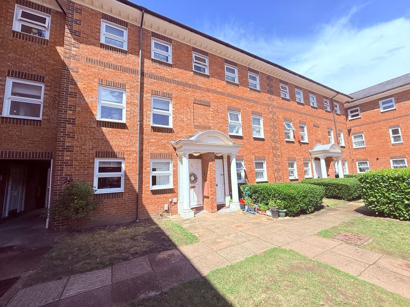 Red brick apartment building with white-framed windows, entrance portico, paved courtyard and manicured lawn
