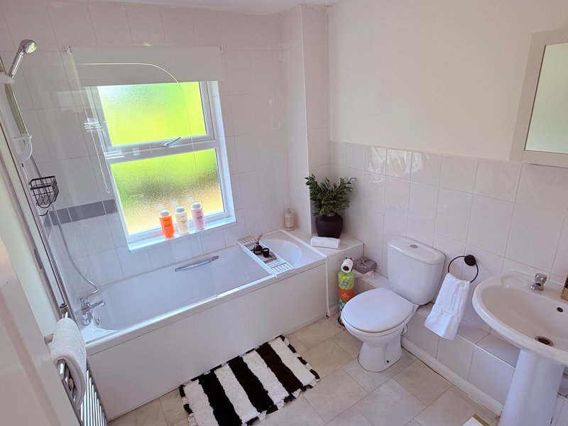 Bright bathroom with bathtub, shower screen, toilet, sink and window overlooking garden