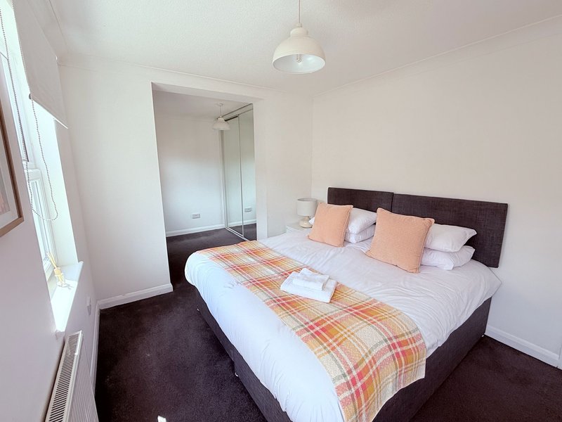 Bedroom with double bed, orange plaid runner, dark headboard and carpet, ensuite visible
