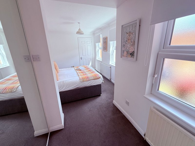 Bright bedroom with double bed, orange bedding, white wardrobe and large windows