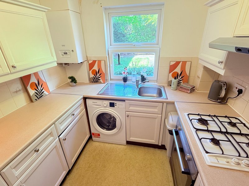 Modern kitchen with white cabinetry, washing machine, gas hob, sink and window overlooking garden