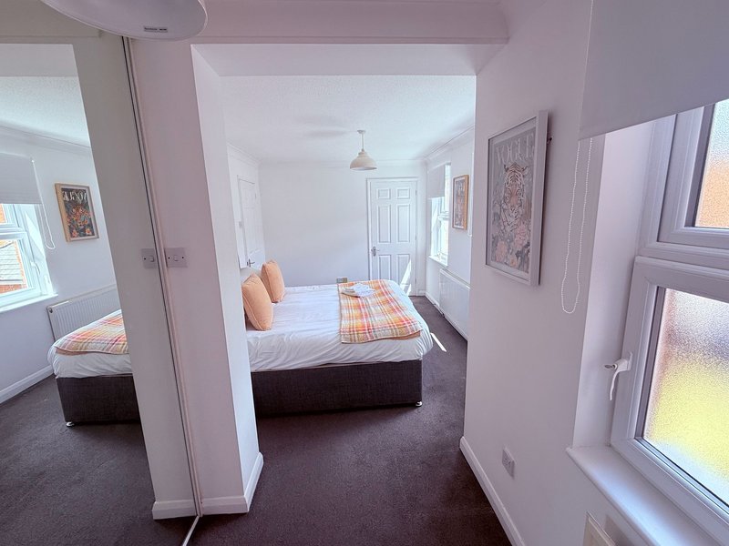 Modern bedroom with double bed, orange pillows, dark carpet, and white walls with artwork
