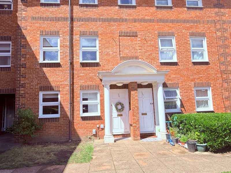 Red brick terraced house exterior with white-framed windows, arched doorway and front garden