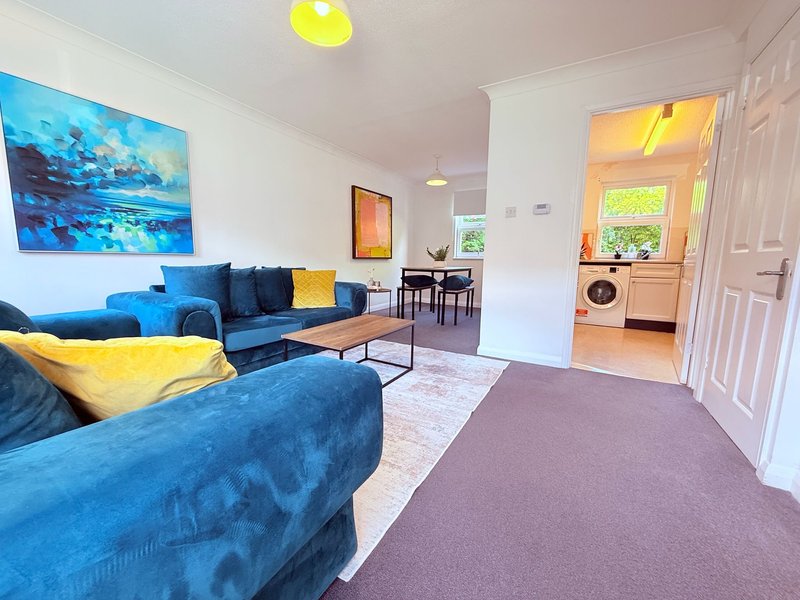 Open-plan living room with blue upholstered sofa, yellow cushions, dining area and kitchen visible through doorway