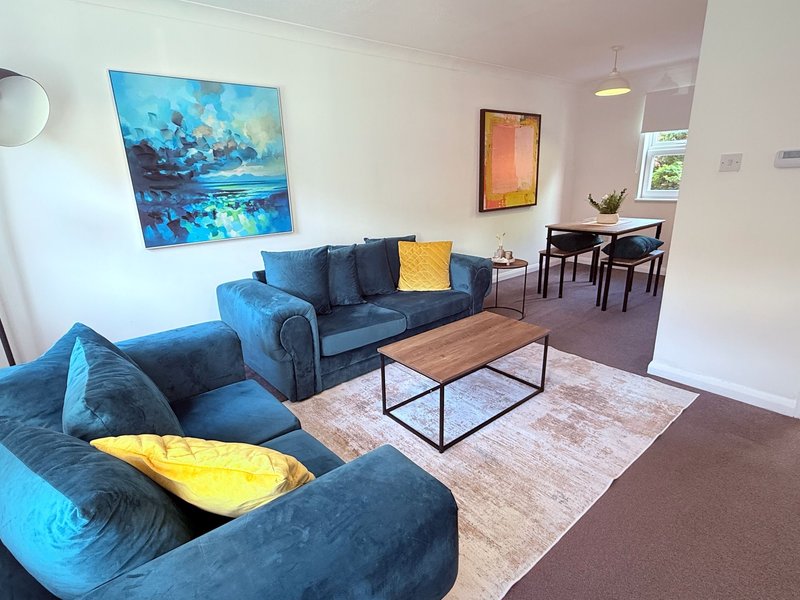 Open-plan living room with blue sofas, wooden coffee table, and framed artwork on walls
