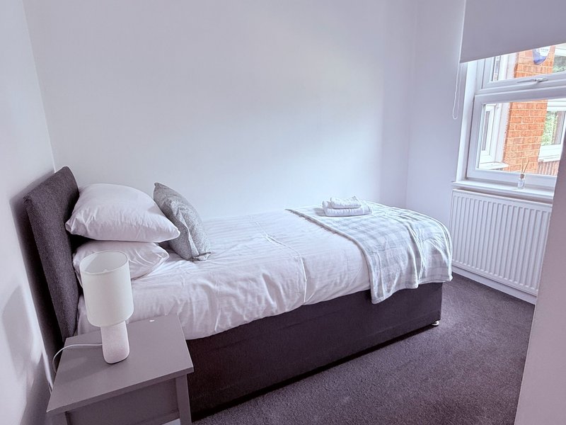 Modest bedroom with single bed, grey headboard, white bedding and small side table
