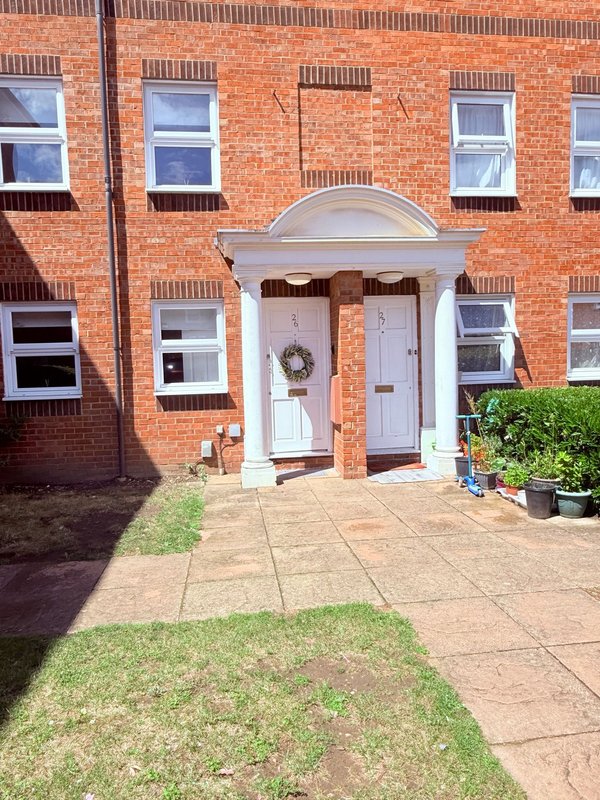 Red brick townhouse with white-framed windows, columned doorway, and paved front courtyard