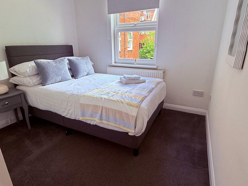 Bedroom with double bed, dark headboard, blue pillows and white bedding, window with exterior view