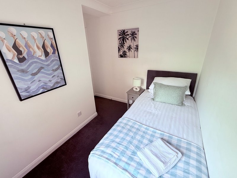 Small bedroom with single bed, dark headboard, bedside table, and framed wall art
