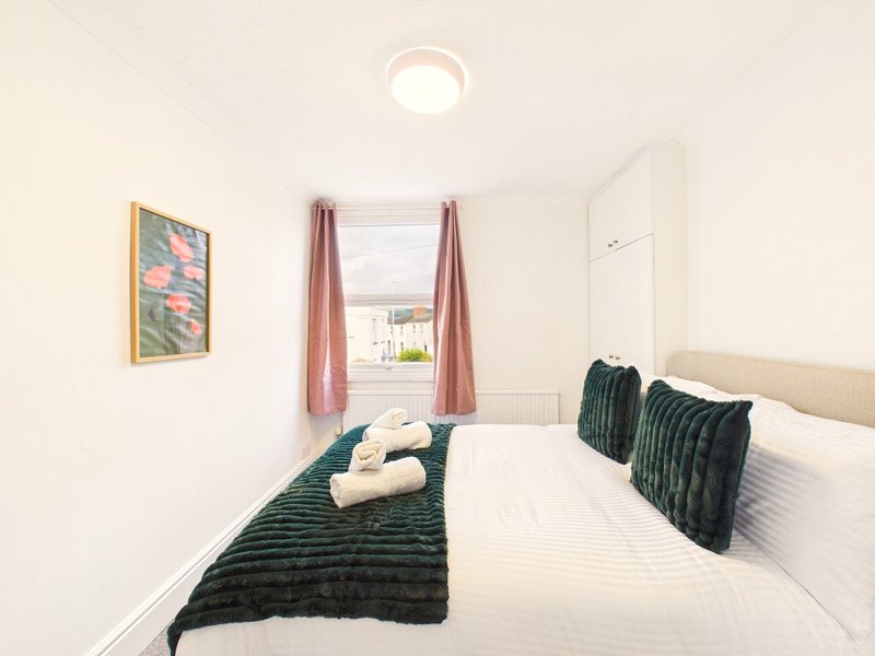 Modern bedroom with double bed, green cushions, white bedding and window with pink curtains