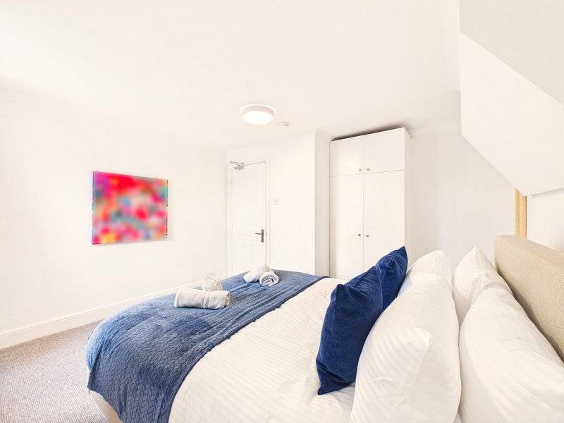 Modern bedroom with double bed, blue bedding, white pillows, and colorful abstract wall art