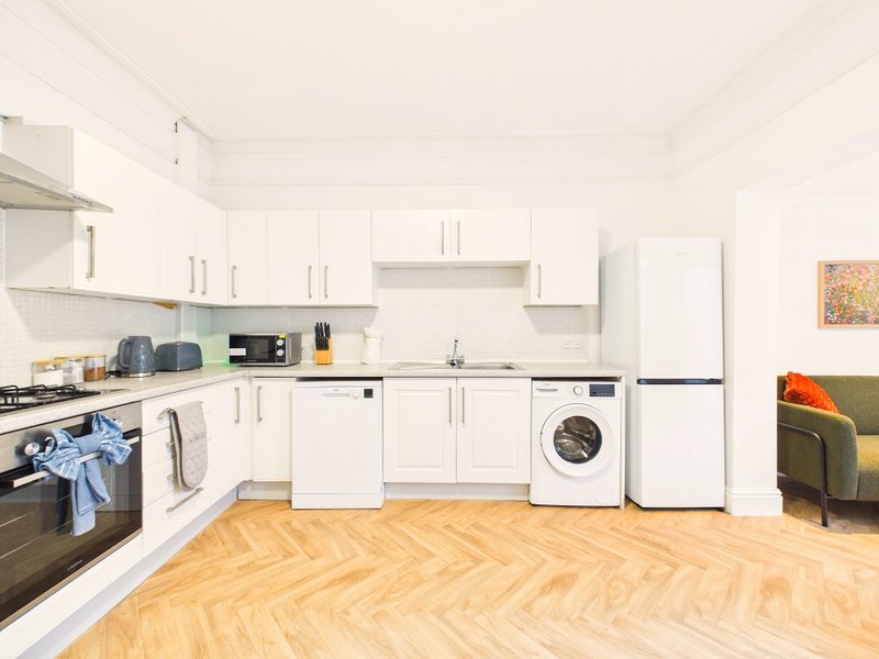Modern kitchen with white cabinets, integrated appliances, wooden herringbone floor and green armchair