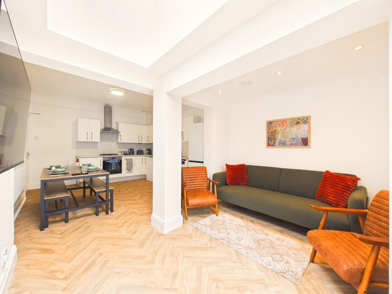 Open-plan living and kitchen area with grey sofa, orange armchairs, wooden flooring and skylight
