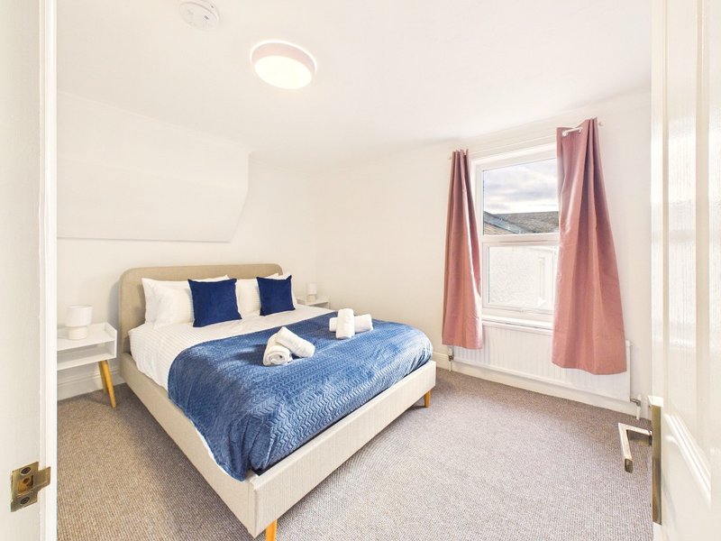 Bright bedroom with double bed, blue bedding, navy pillows, and pink curtains framing window