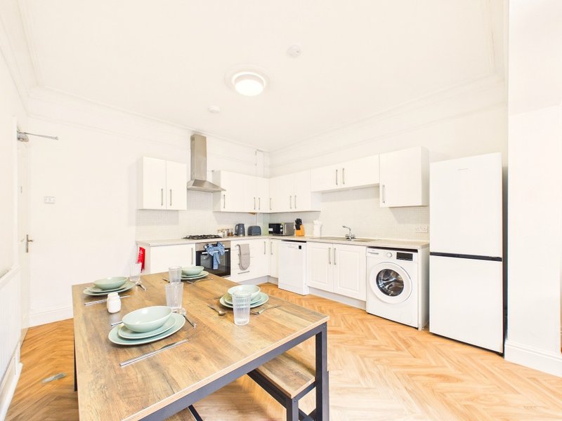 Modern kitchen with white cabinets, wooden dining table, stainless steel appliances and parquet flooring