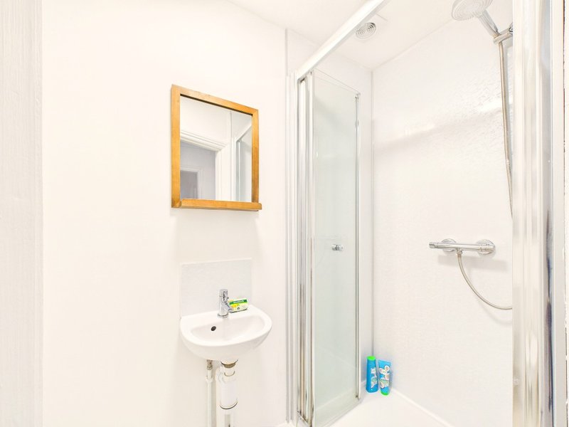 Clean white bathroom with wall-mounted sink, wooden-framed mirror, and glass shower enclosure