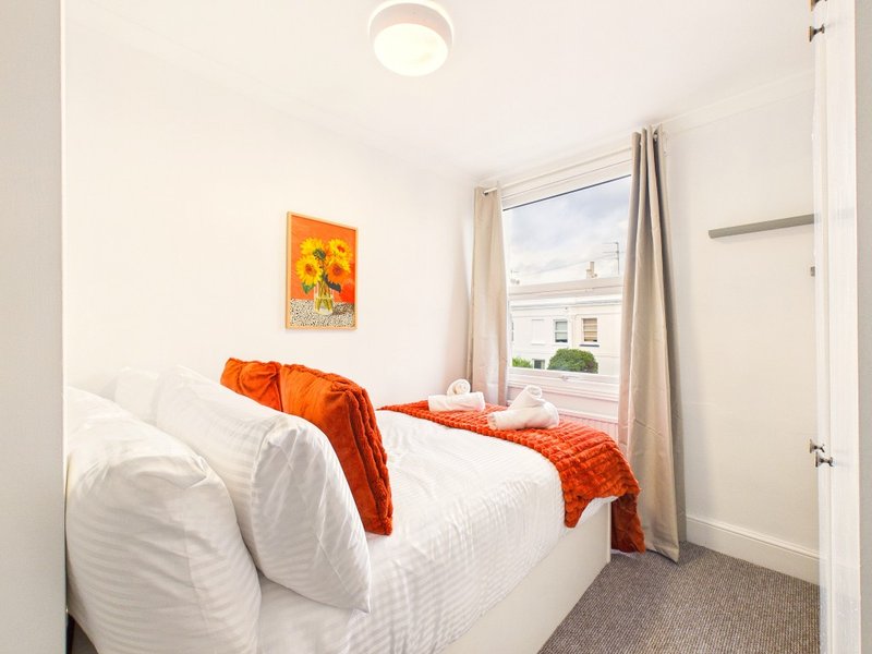 Bright bedroom with double bed, white bedding, orange throw blanket and artwork on wall