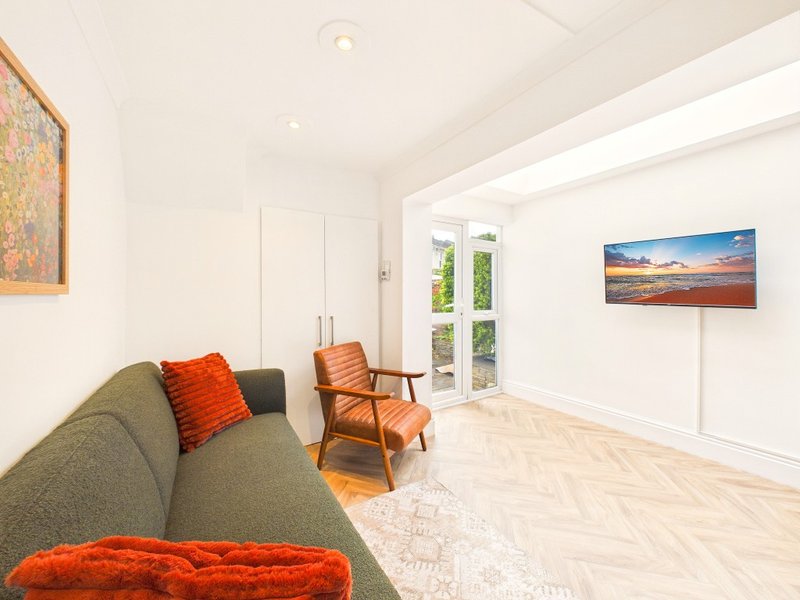 Bright modern living room with green sofa, orange cushions, wooden chair and patio doors