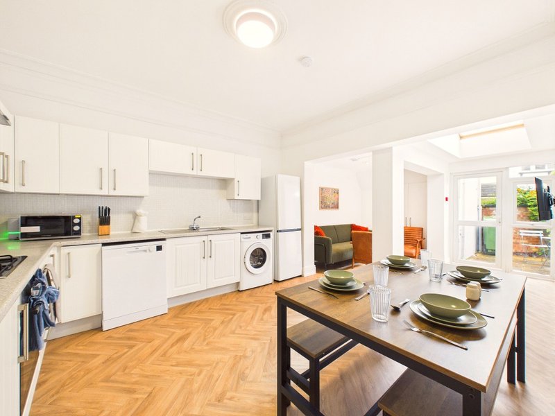Modern kitchen with white cabinetry, wooden flooring, dining table and open-plan living area