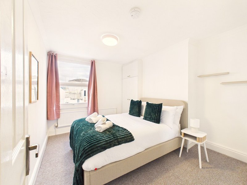Bright modern bedroom with double bed, teal bedding, window with pink curtains and city view