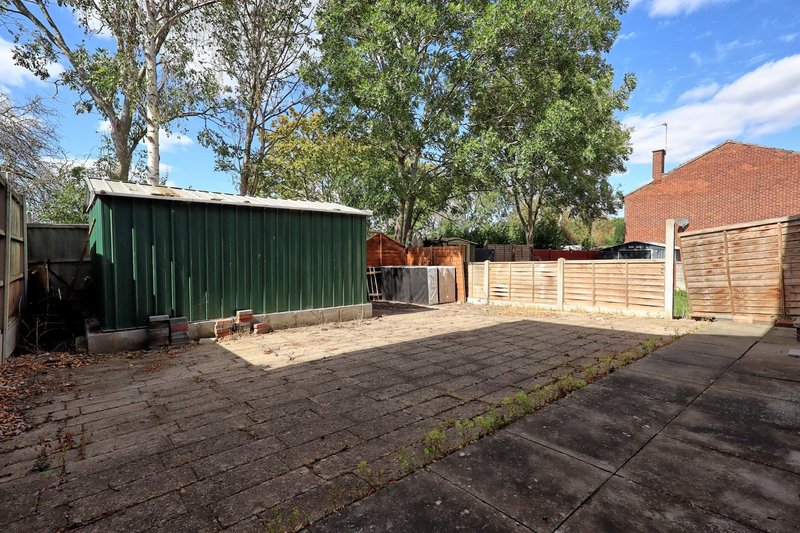 Rear garden with paved patio, wooden fence, green shed and brick house visible