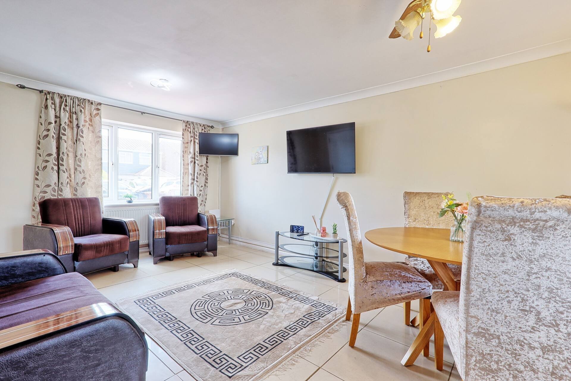 Spacious living room with seating area, two wall-mounted TVs, window with curtains, and wooden furniture