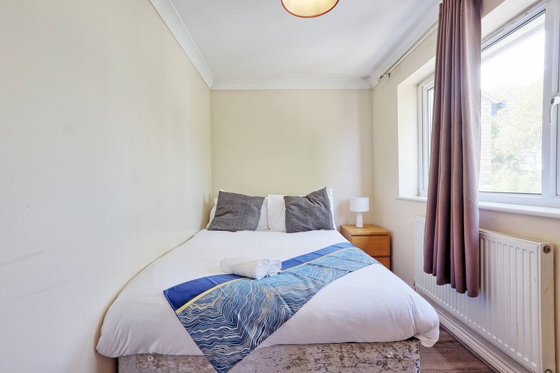 Compact bedroom with double bed, blue bedding, wooden nightstand and window with purple curtains