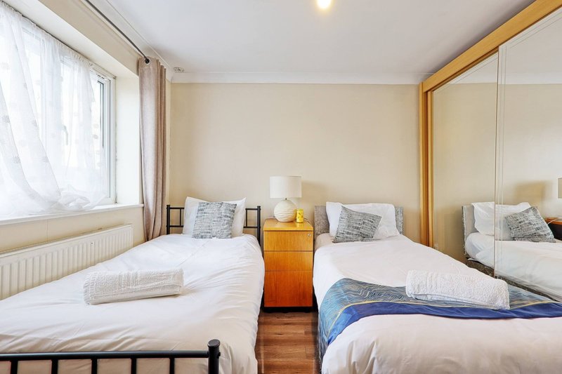 Bright bedroom with two single beds, wooden nightstand, mirror, and large window with curtains