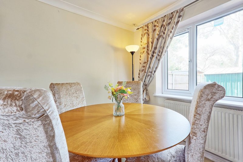 Dining area with round wooden table, upholstered chairs, and large windows overlooking garden