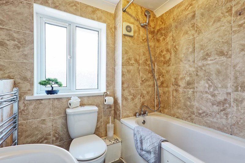 Bathroom with toilet, bathtub, shower enclosure, window and beige tile walls