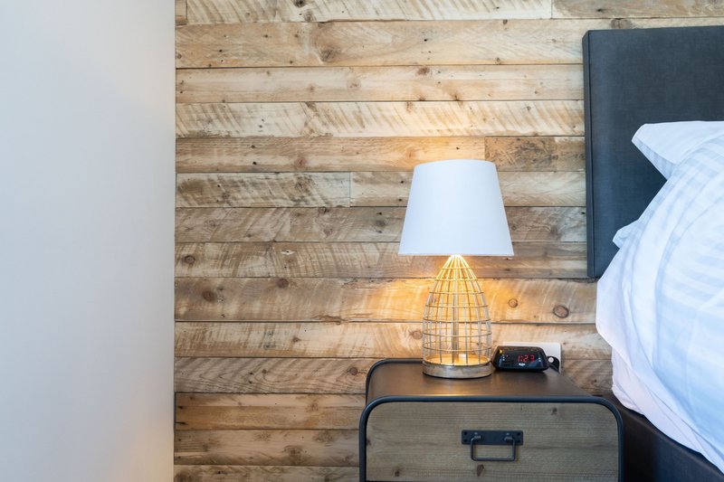 Bedroom bedside table with table lamp, dark headboard, and wooden accent wall