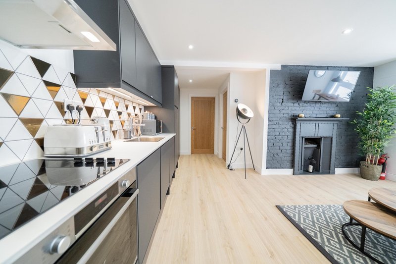 Modern open-plan kitchen and living room with dark cabinetry, geometric tile backsplash, wooden flooring and fireplace