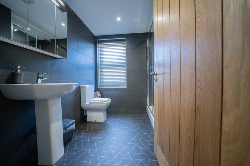 Modern bathroom with pedestal sink, toilet, shower enclosure and blue tile flooring
