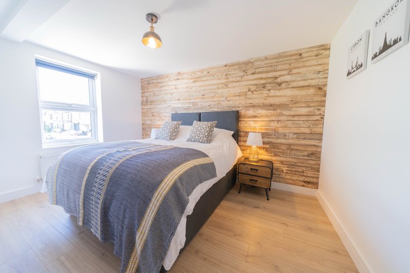 Bedroom with double bed, wooden feature wall, wooden floor and bedside lamp