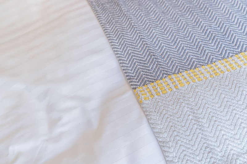 Close-up of bedding with white sheet and gray patterned throw with yellow trim