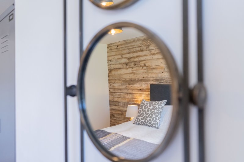Bedroom reflected in round mirror, showing bed with patterned pillow and brick wall