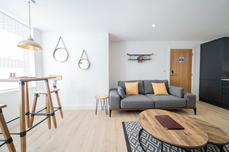 Open-plan living room with grey sofa, wooden dining table, kitchen area and decorative wall mirrors