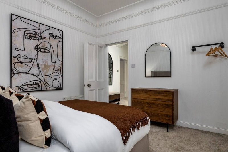 Modern bedroom with double bed, wooden dresser, abstract wall art, and arched mirror