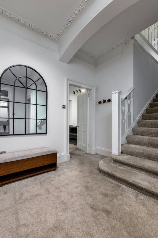 Bright entrance hall with arched window, wooden bench, staircase and white walls