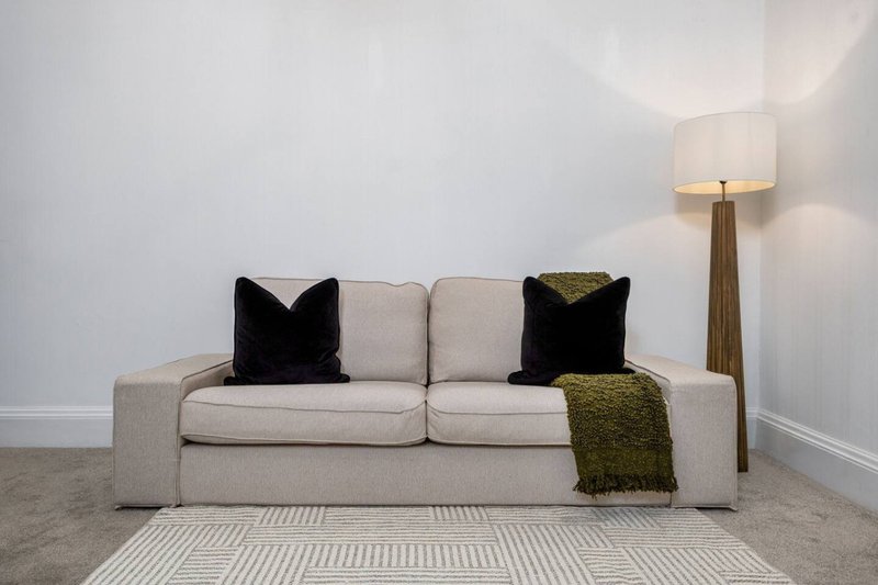 Modern living room with beige sofa, black velvet cushions, olive throw, and wooden floor lamp