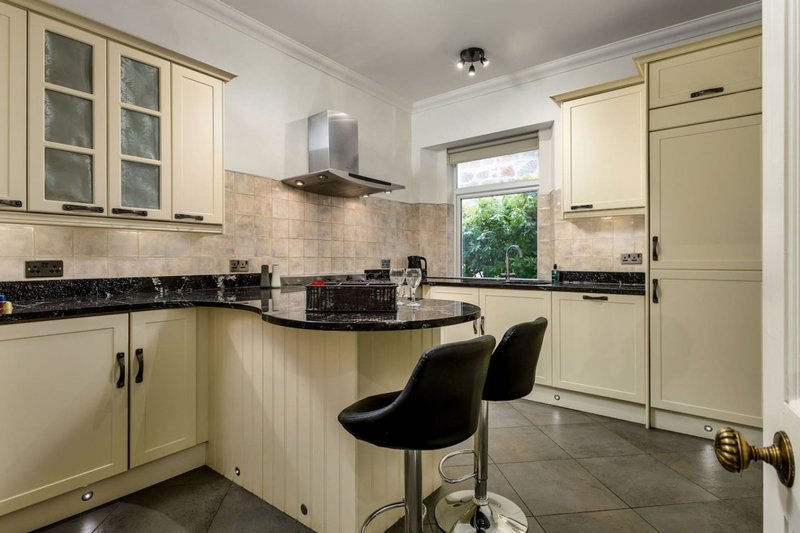 Modern cream kitchen with black countertops, island seating, and stainless steel appliances