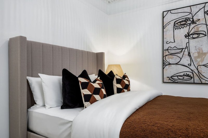 Modern bedroom with grey upholstered headboard, white bedding, decorative pillows and abstract wall art