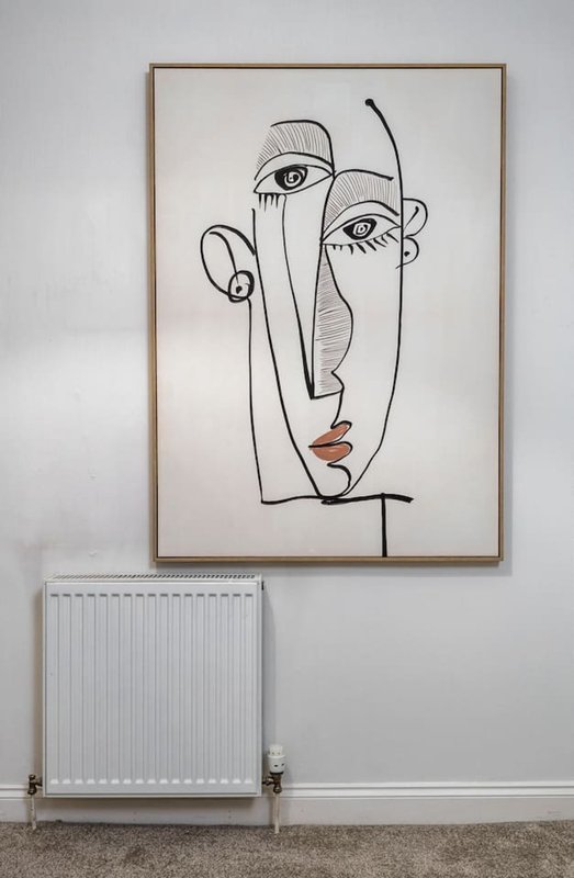 White wall with framed abstract line art portrait above white radiator