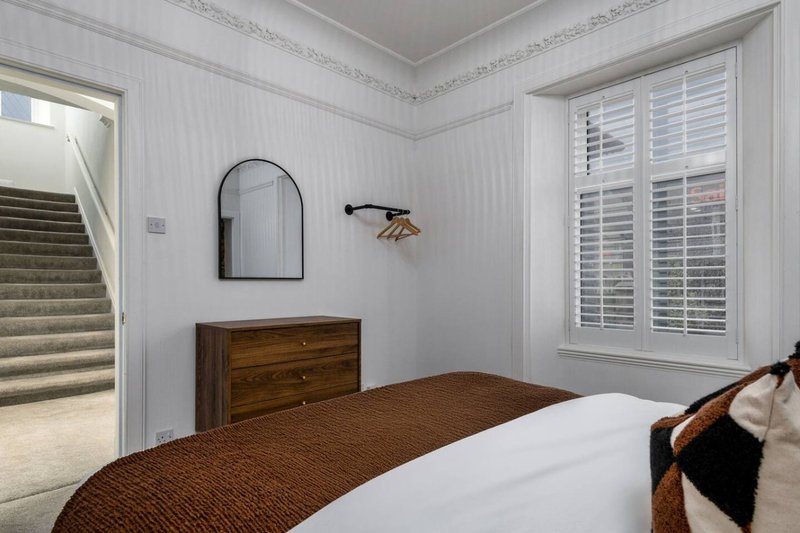 Bright bedroom with double bed, wooden dresser, arched mirror, and shuttered windows