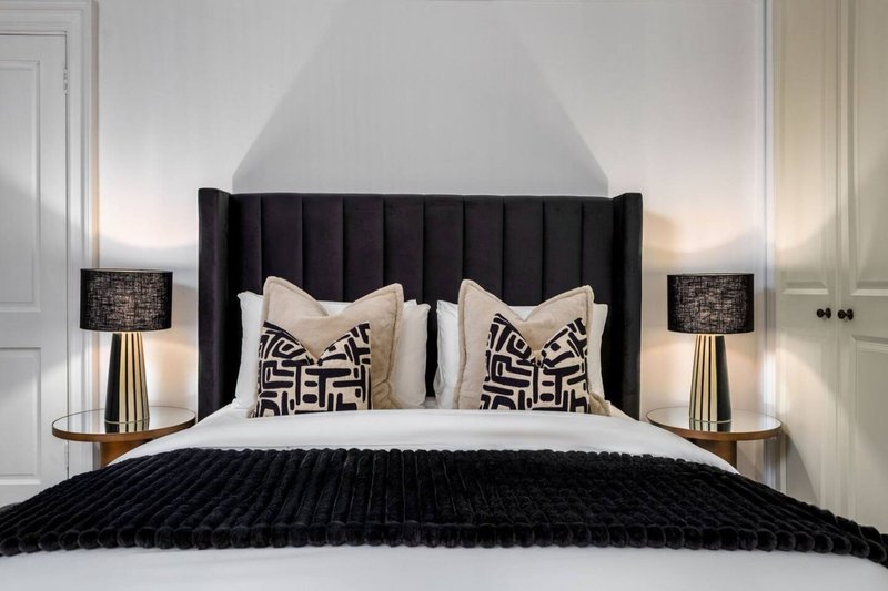Modern bedroom with black padded headboard, white bedding, geometric pillows and black throw blanket