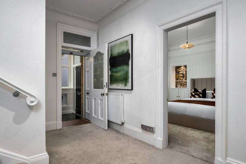 Hallway with white walls, carpet flooring, framed landscape artwork, and open doorways