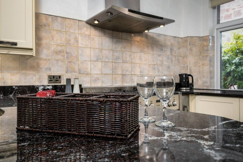 Modern kitchen with black granite countertop, tiled backsplash, wine glasses, and wicker basket storage