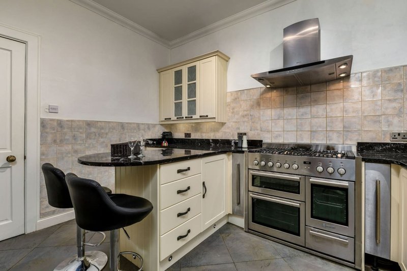Modern kitchen with cream cabinetry, black granite countertops, stainless steel range cooker and extractor hood