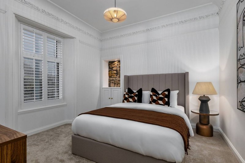 Modern bedroom with grey upholstered bed, white bedding, wooden nightstand and pendant ceiling light